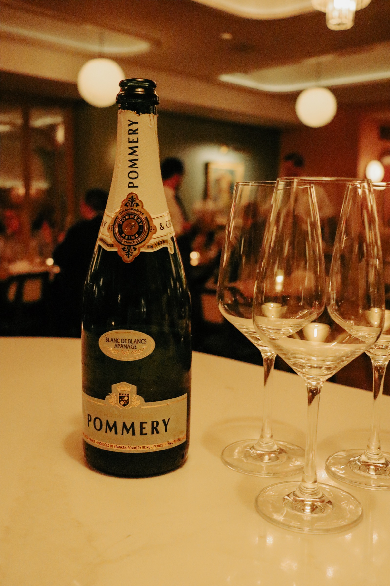 A bottle of champagne and glasses on the bar with the dining room beyond