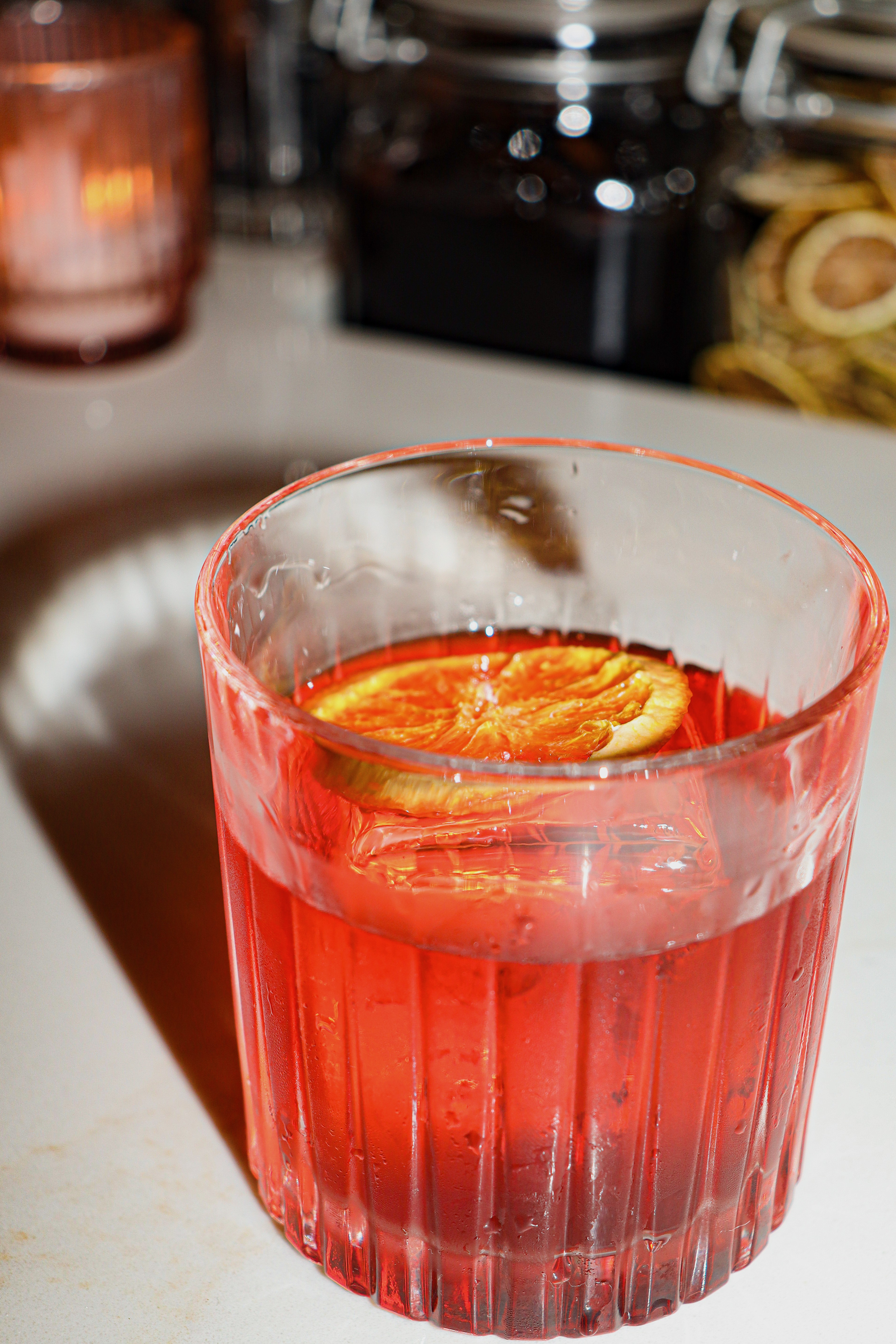 A Negroni with dried orange slice and warm votive glow